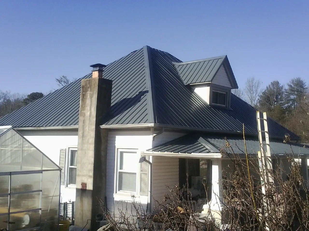 Dark blue standing seam metal roof on a white farmhouse with dormer — Slate & Tile Roof Repair by Roofing Brothers in Englewood