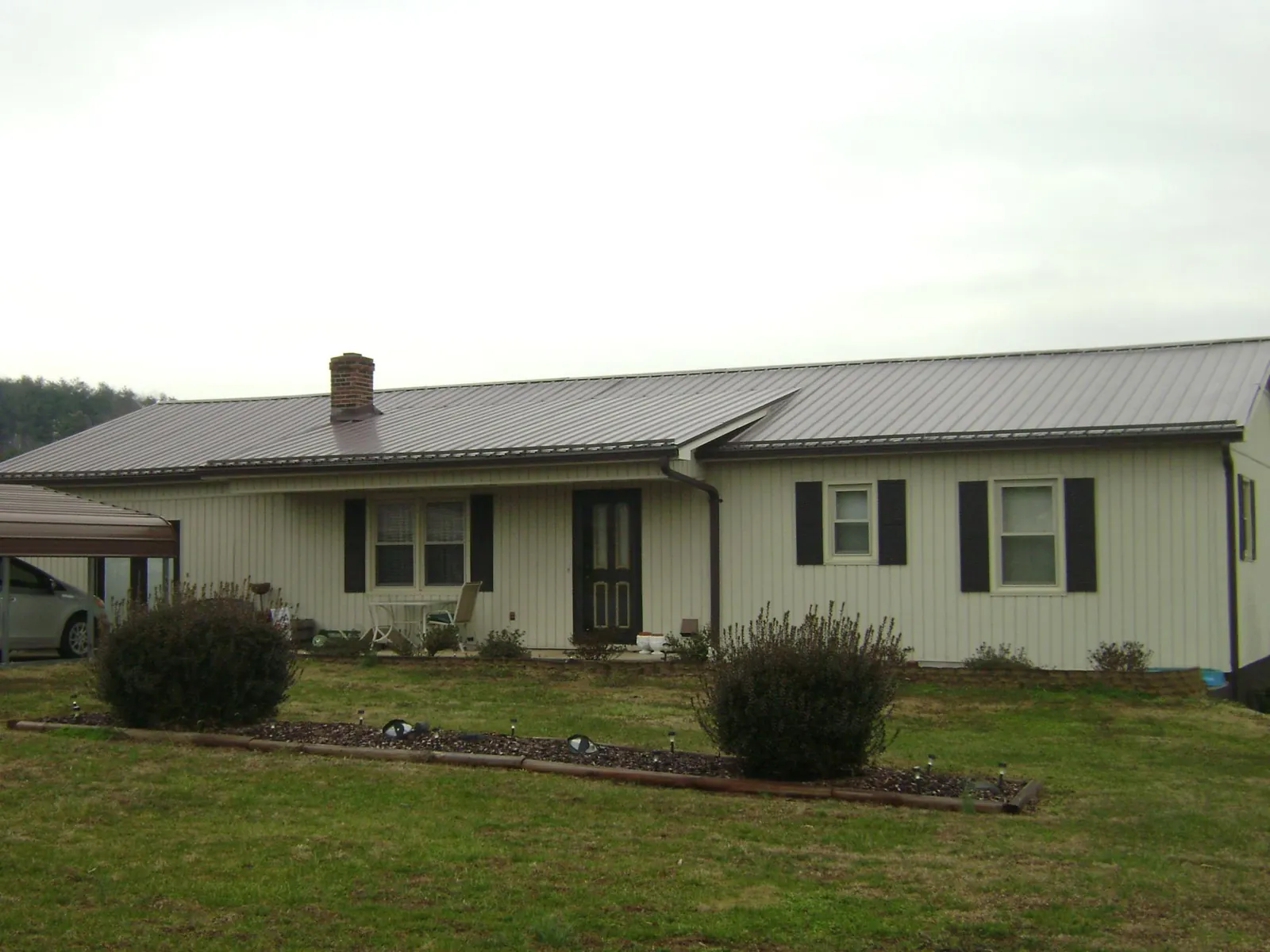 Brown metal roof on a cream sided ranch home with a brick chimney in Englewood